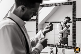 In an Austrian hotel room, the groom fixes his cufflinks, captured in a black-and-white image of him reflected in the bathroom mirror while preparing for the wedding.